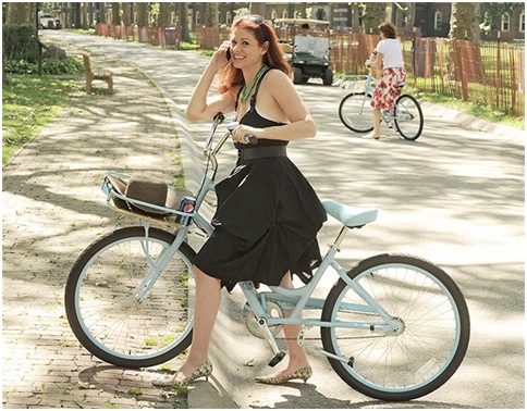 Debra Messing bersepeda dengan menggunakan gaun dansepatu flatshoes.